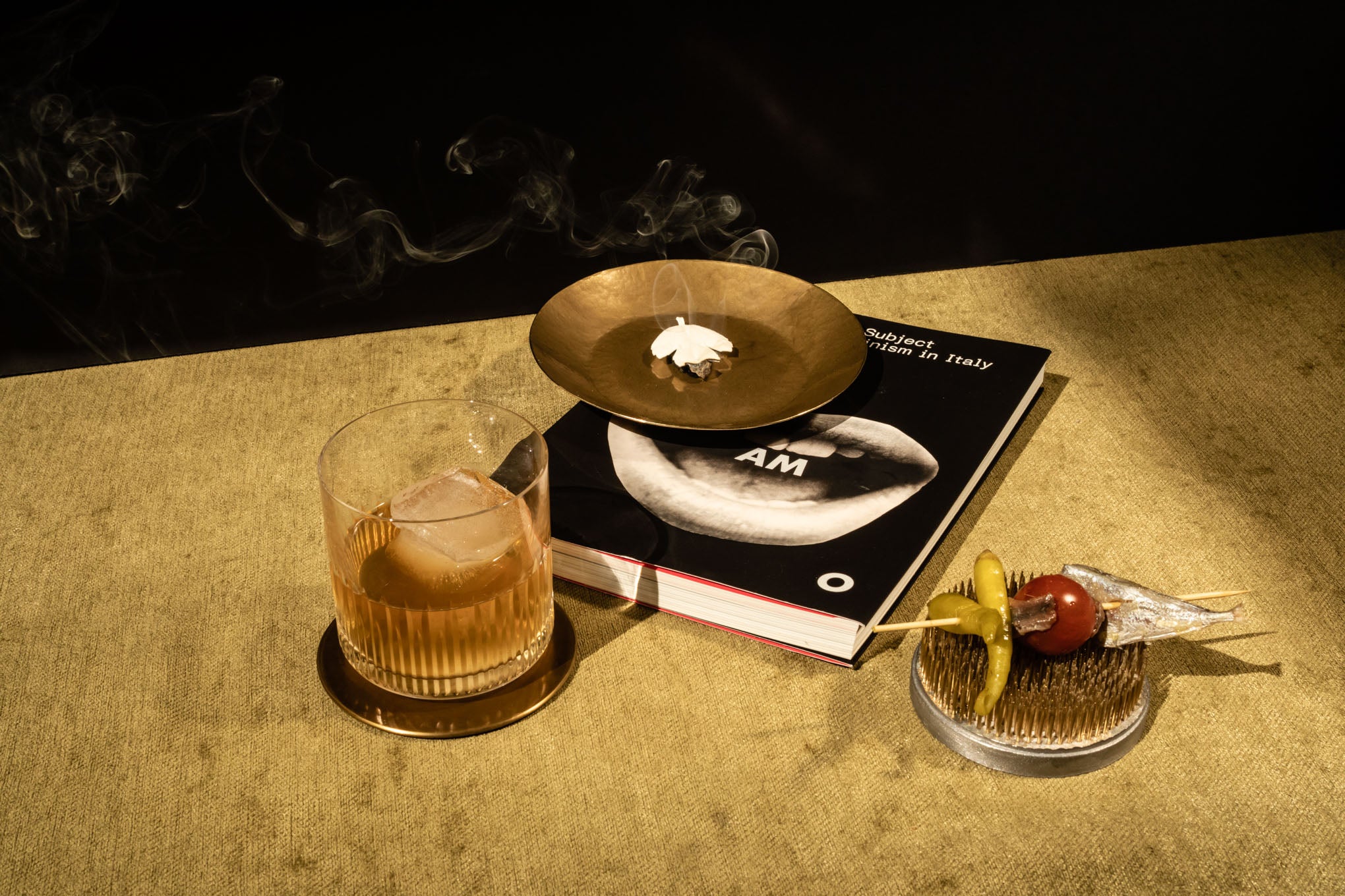 Glass of liquor, burning white leaf, book, and peppers on a table 