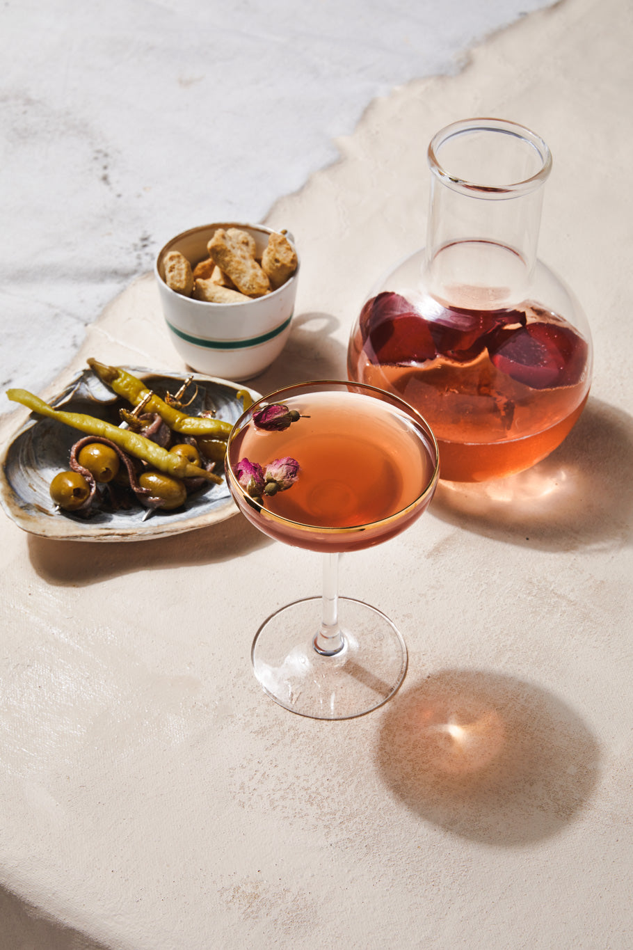 pink martini in glass with rosebuds, cocktail decanter with rose petals and skewers with olives and guindillas