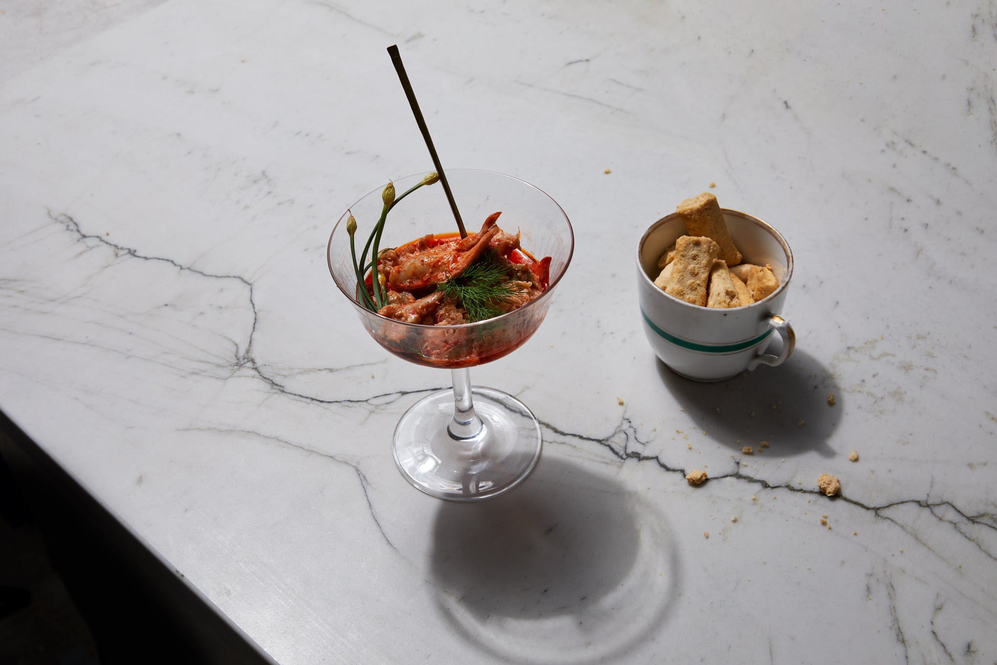 lobster in martini glass with brass spoon and cup of biscuits