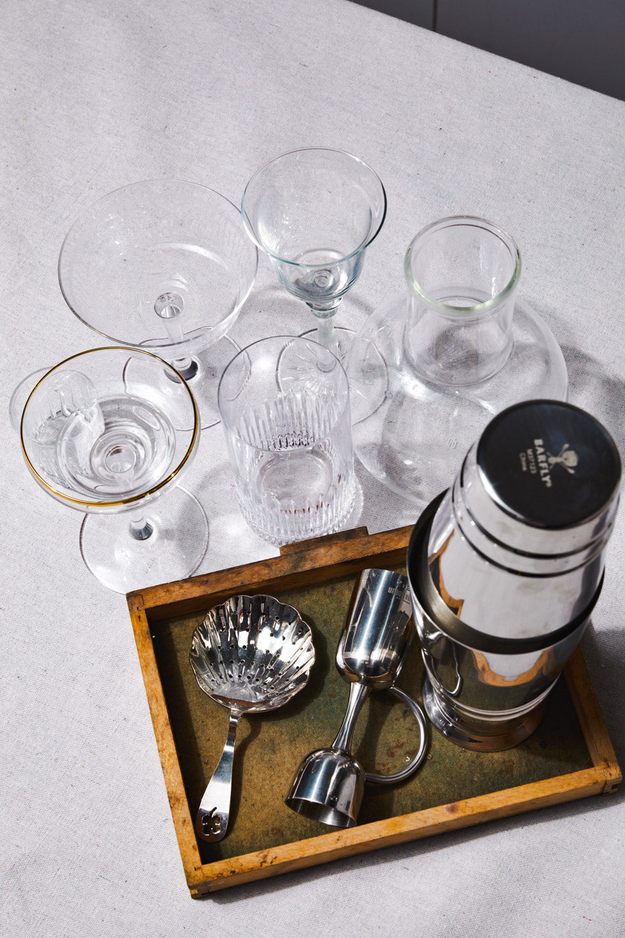 various empty cocktail glasses next to silver plated strainer, coley jigger and cocktail shaker set
