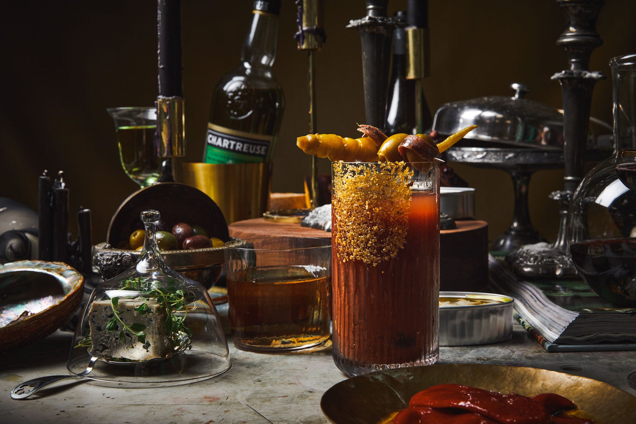 A bloody Mary prepared in a tall clear etched glass with truffle lemon olive gold sugar salt pressed into the side
